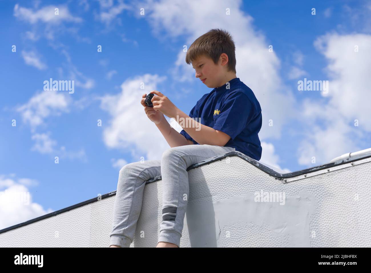 Ein Junge sitzt auf dem Dach eines Lieferwagens unter einem wunderschönen blauen Himmel und fotografiert Stockfoto