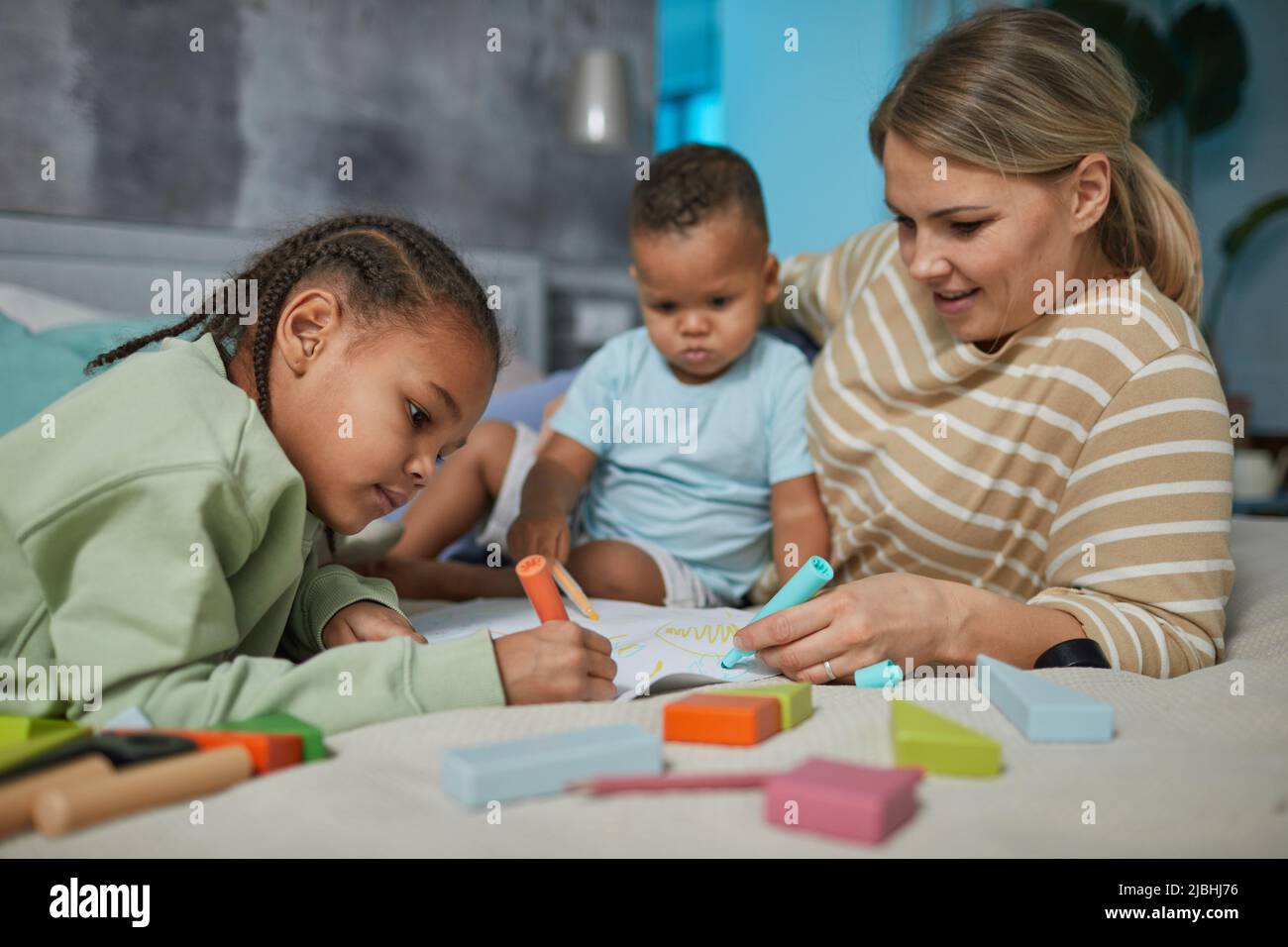Porträt einer glücklichen kaukasischen Mutter mit zwei afroamerikanischen Kindern, die zusammen auf dem Bett liegen Stockfoto