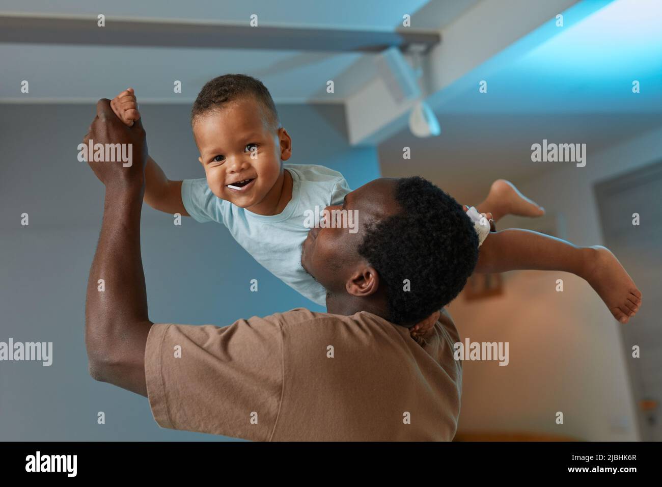 Porträt des glücklichen schwarzen Vaters, der mit niedlichem Baby zu Hause spielt und lächelnden Sohn in der Luft hält Stockfoto