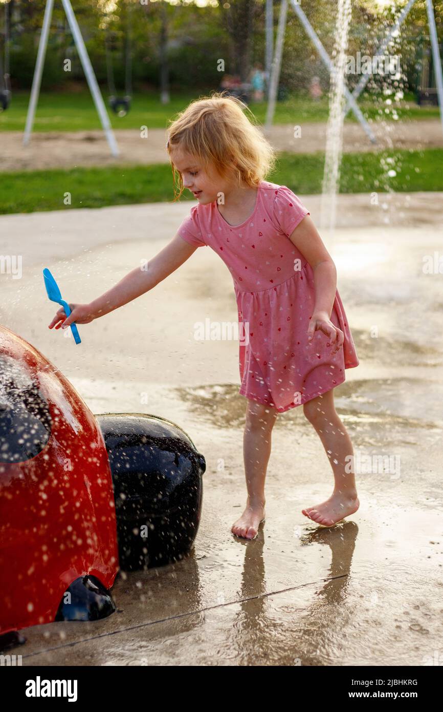 Im Sommer spielt ein kleines, glückliches Kind auf dem Splash-Pad-Spielplatz. Wasserpark mit Springbrunnen für Kinder. Sommeraktivitäten für Kinder Stockfoto