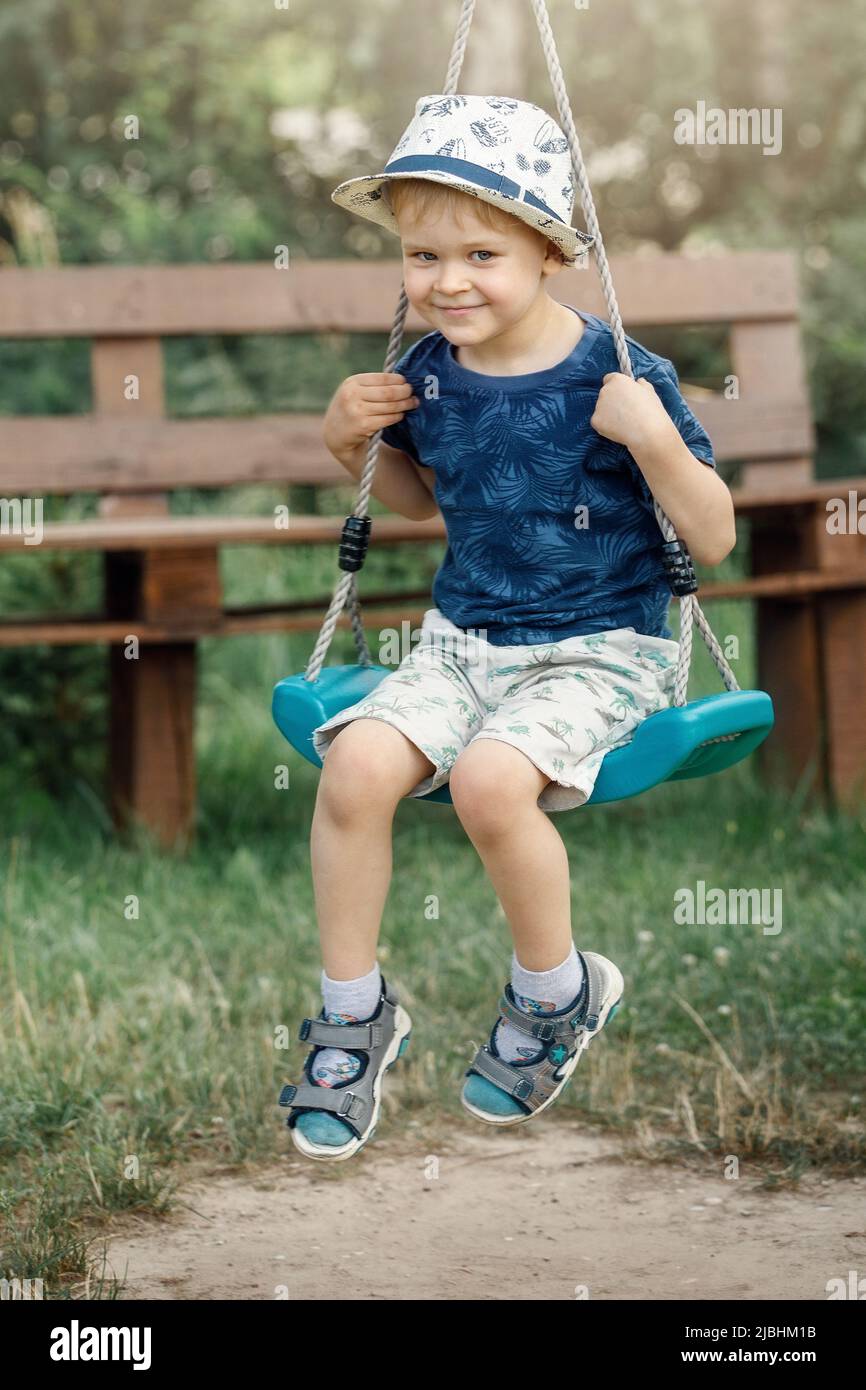 Sehr glückliches Kind, in den Ferien im Sommergarten der Großmutter zu schaukeln. Stockfoto