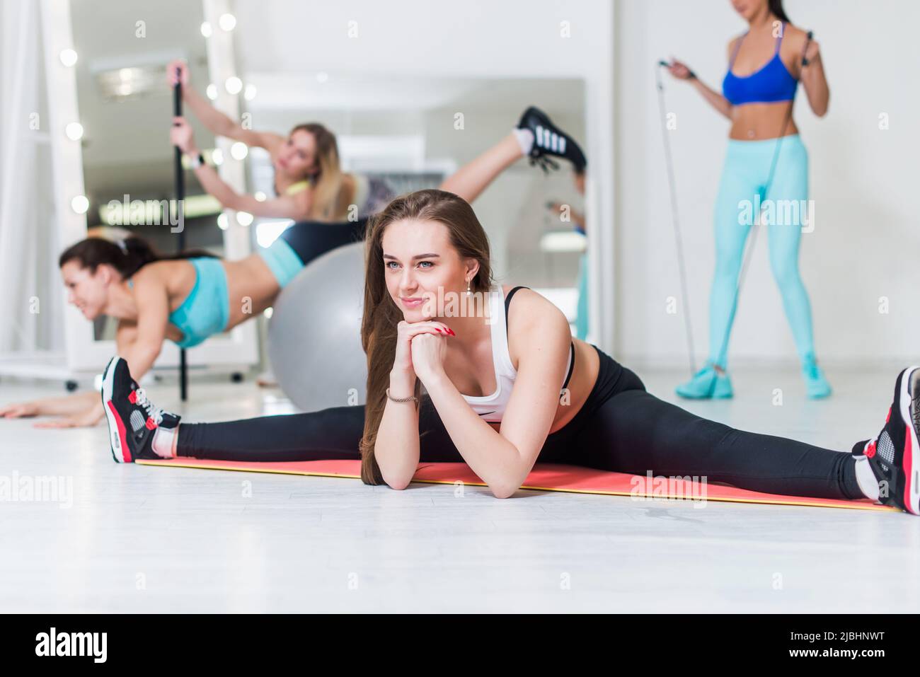 Sportliche Frauen, die im Fitnessstudio verschiedene Fitnessübungen machen Mädchen, die im mittleren Spalt sitzen und ihre inneren Oberschenkel auf dem Boden im Sportverein strecken. Stockfoto