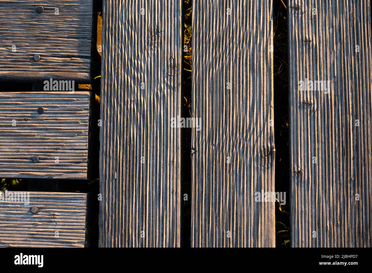 Ein Spiel von Lichtern und Schatten auf den Brettern eines hölzernen Piers. Das Licht, das in einem hohen Winkel auf die Bretter fällt, betont die Struktur des Materials Stockfoto