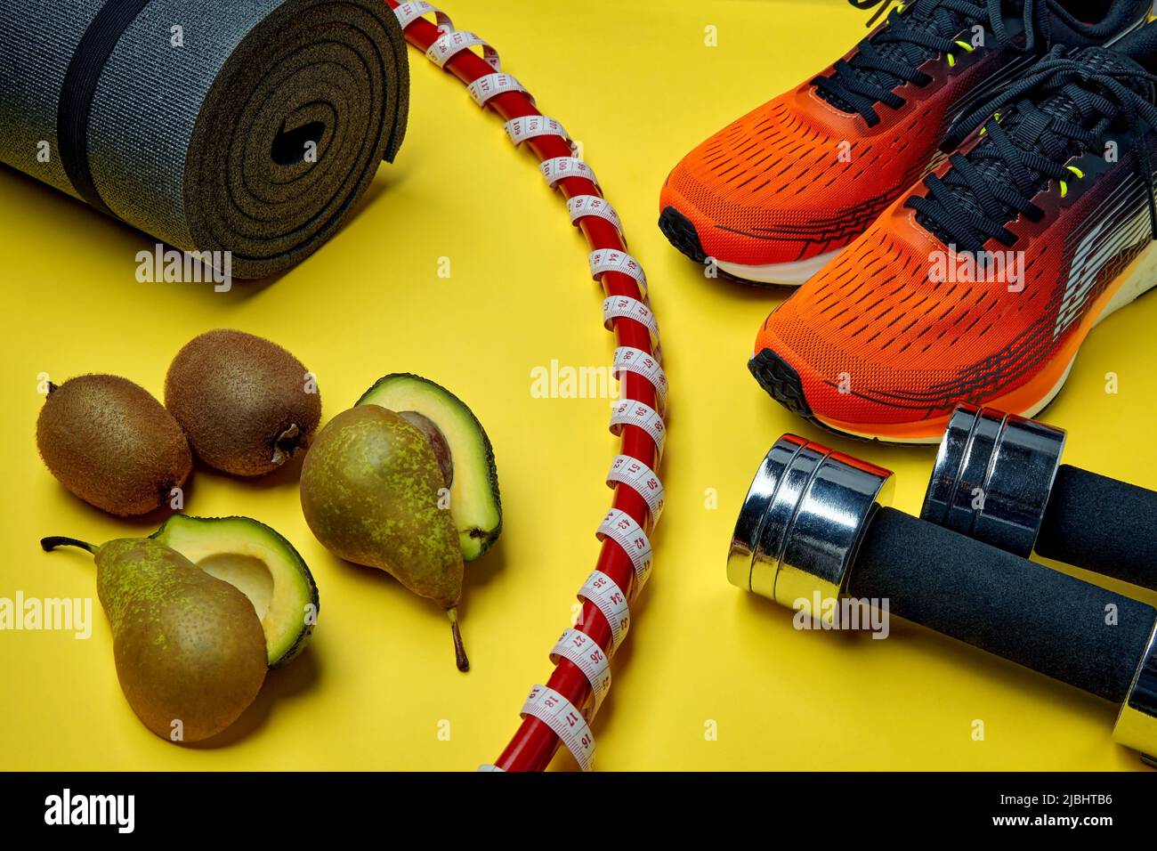 Abnehmen und Gesundheit Bewegung und Ernährung Konzept. Orangefarbene Sportschuhe, Turnring in ein Maßband mit einem Meter eingewickelt, Hanteln, Yoga und Stockfoto