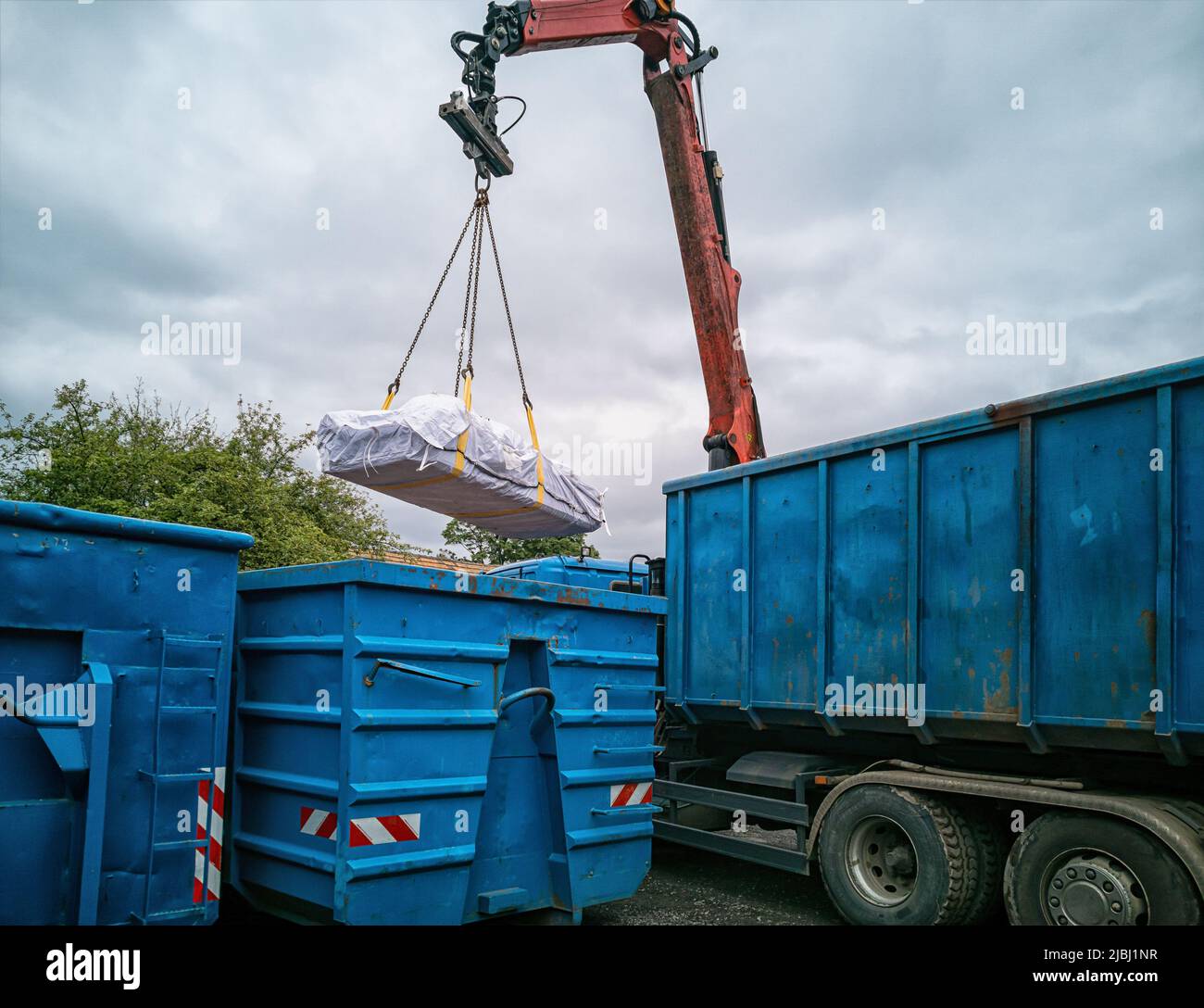 Kranwagen mit Asbestbeutel, der auf einem Recyclinghof in einen anderen Container geladen wird. Stockfoto