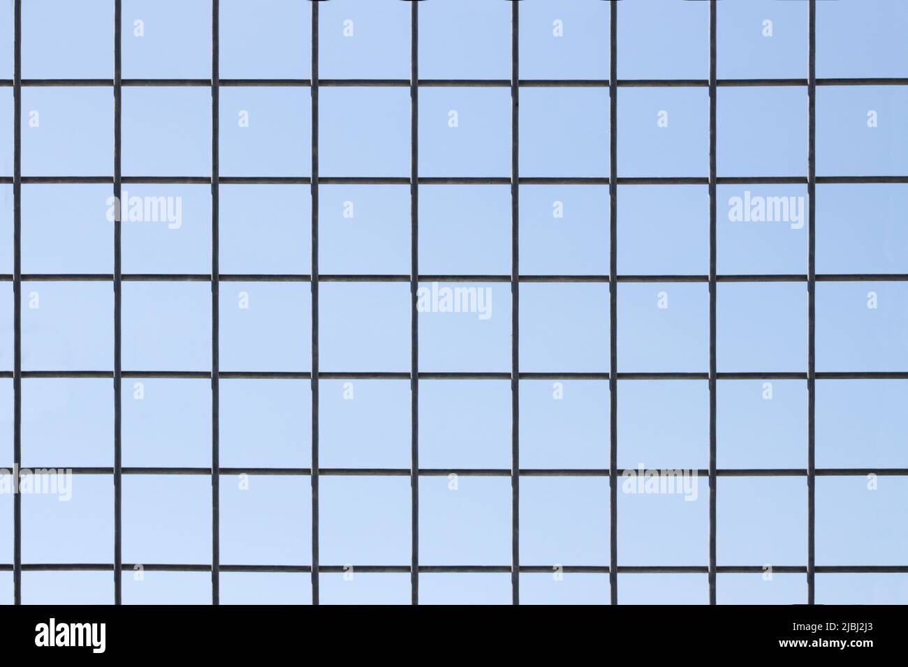 Nahaufnahme eines Zauns, dessen Draht perfekte Quadrate bildet, mit dem blauen Himmel im Hintergrund Stockfoto