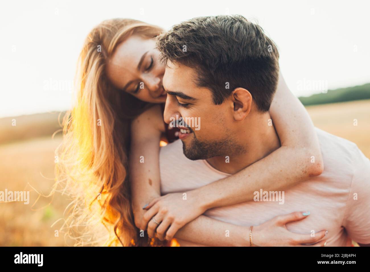 Porträt eines lächelnden, gutaussehenden Mannes, der seiner ginger Freundin eine Schweinegride im Weizenfeld gab. Wunderschönes Porträt. Freizeitaktivitäten. Sommer Stockfoto