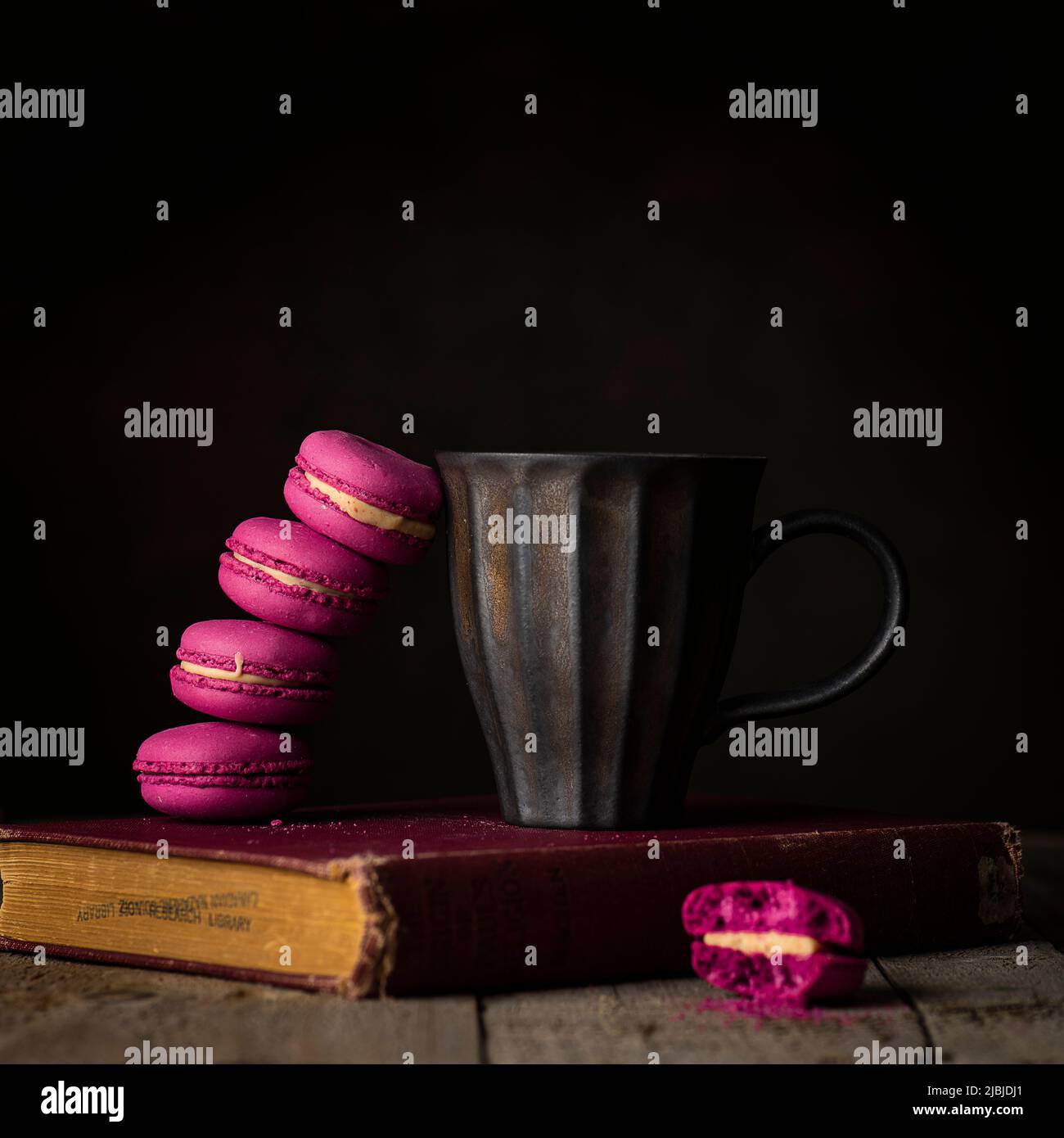 Erdbeer-Macaron mit antiker Kaffeetasse oben auf altem Buch Stockfoto