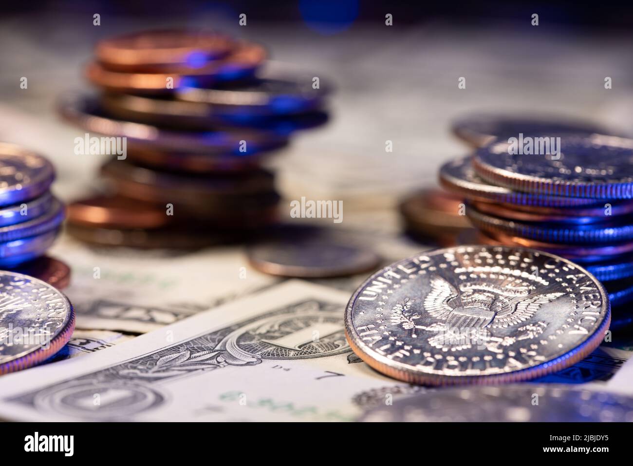 Eine halbe Dollar-Münze mit Adler, daneben stapelten wir Dollar-Münzen, die über 1 usd-Scheine emporragten. Dollar-Banknoten als Hintergrund. Wirtschaft und Wohlstand in der Stockfoto