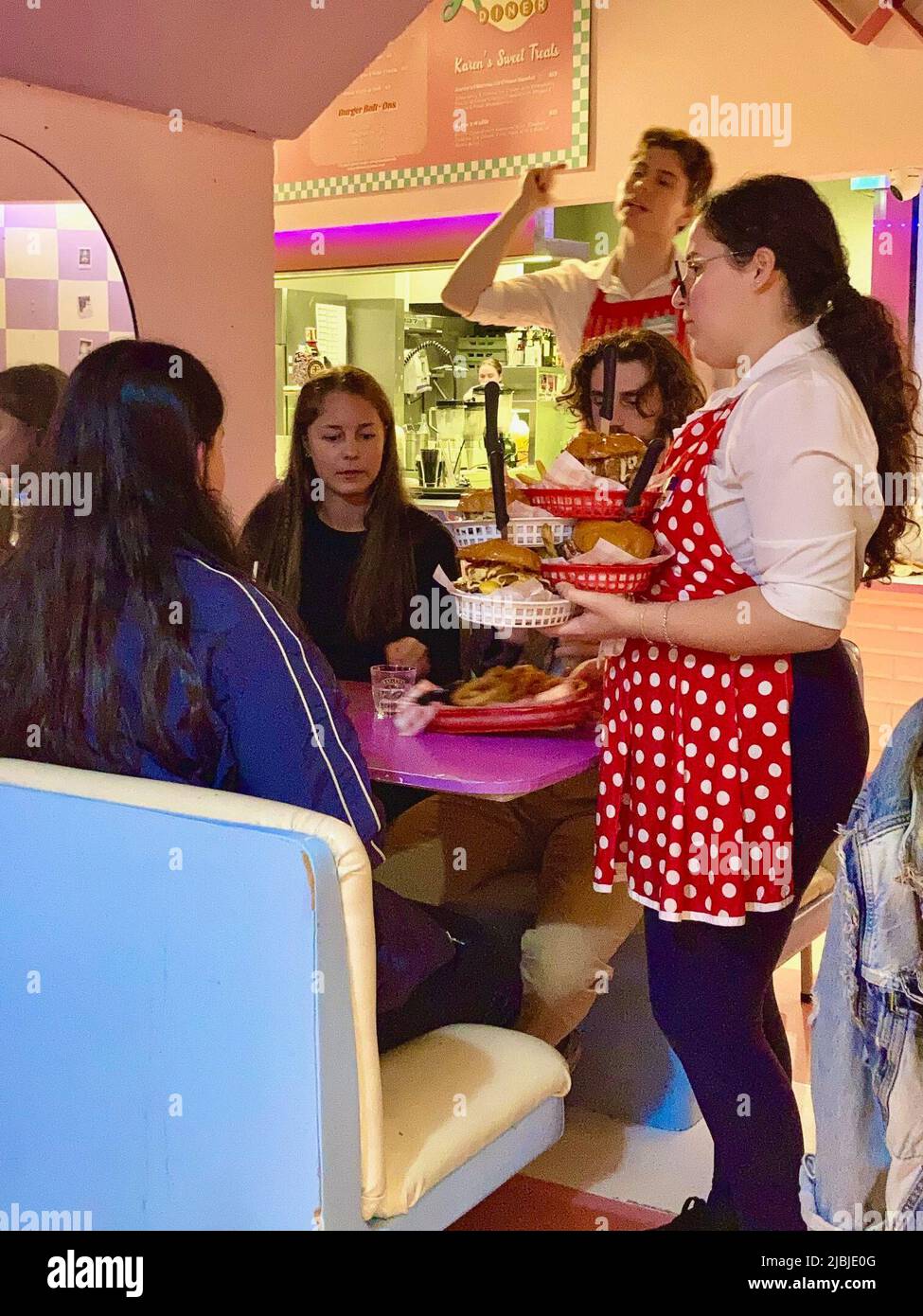 Sydney, Australien. 25.. Mai 2022. Eine leicht verärgerte Kellnerin in rot-weißer Schürze serviert Burger und Pommes im Karen's Diner. Restaurants sind in der Regel stolz auf guten Service. Nicht so bei Karen's Diner in Australien, wo die Gäste mobbt und extra schlecht bedient werden. Das kuriose Konzept wird so gut angenommen, dass die Kette nun weltweit expandiert. (To dpa 'unhöfliche Kellner als Erfolgsrezept: Karen's Diner erobert Australien') Quelle: Carola Frentzen/dpa/Alamy Live News Stockfoto