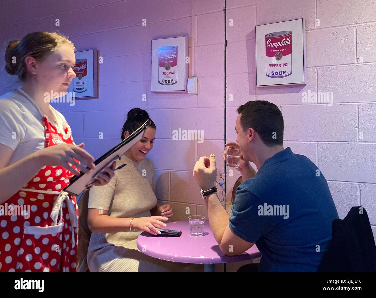 Sydney, Australien. 25.. Mai 2022. Eine leicht verärgerte Kellnerin in rot-weißer Schürze nimmt die Bestellung bei Karen's Diner an. Die Gäste lachen, denn das ganze soll vor allem Spaß machen. Restaurants sind in der Regel stolz auf guten Service. Nicht so im australischen Karen's Diner: Hier werden die Gäste mobbt und extra schlecht bedient. Das kuriose Konzept wird so gut angenommen, dass die Kette nun weltweit expandiert. (To dpa 'unhöfliche Kellner als Erfolgsrezept: Karen's Diner erobert Australien') Quelle: Carola Frentzen/dpa/Alamy Live News Stockfoto