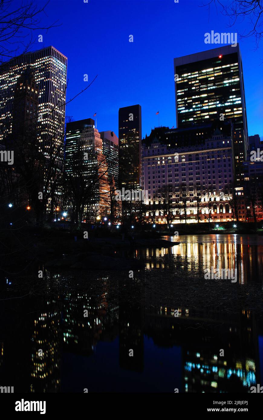 Die Lichter von Manhattan spiegeln sich in einer klaren Winternacht im Wasser des Pond im Central Park von New York City wider Stockfoto