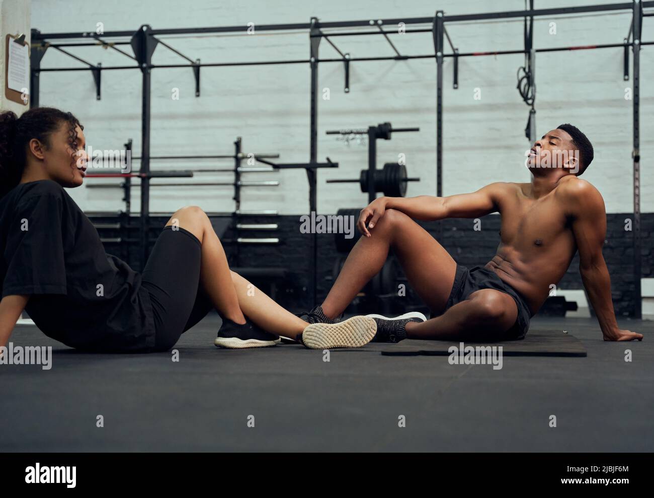 Mixed-Race-Freunde, die im Fitnessstudio Cross-Fit machen. Afroamerikanische Männer und Frauen ruhen nach dem Training auf dem Boden. Hochwertige Fotos Stockfoto
