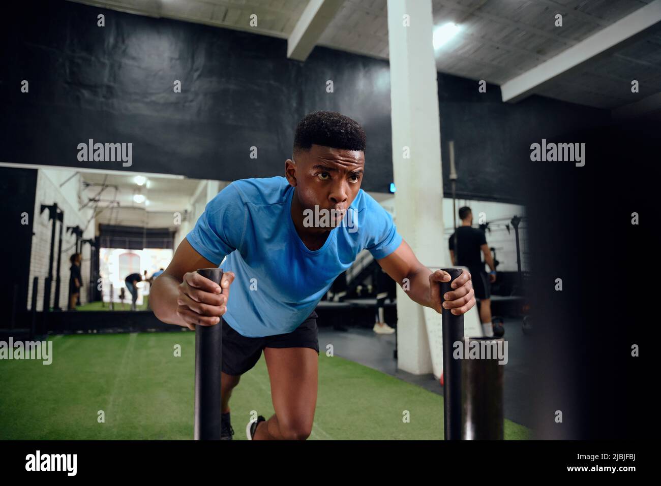 Afroamerikanischer Mann arbeitet intensiv während des Cross-Fit-Trainings. Männlicher Athlet, der den Schlitten im Fitnessstudio schiebt. Hochwertige Fotos Stockfoto