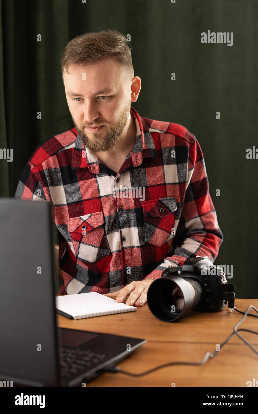 Professioneller Fotograf mit Kamera und Laptop im Studio. Fotograf mit Assistent, der im Büro sitzt und die Kamera anschaut Stockfoto