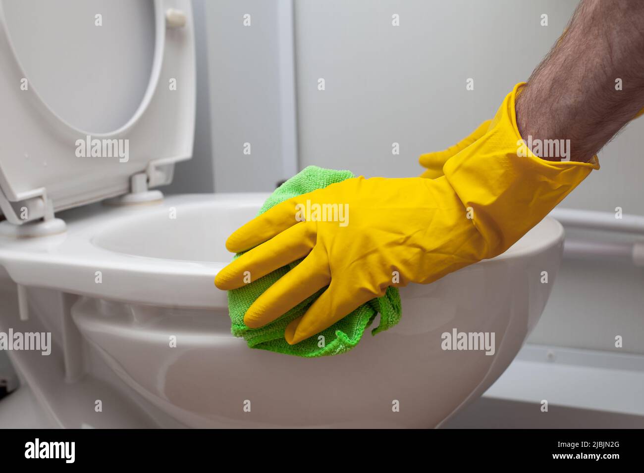 Der Mann reinigt eine Toilette im Badezimmer mit einer grünen Bürste Stockfoto