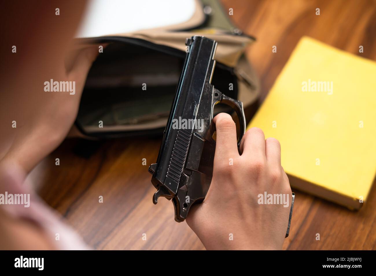 Konzentrieren Sie sich auf die Waffe, Nahaufnahme eines Kindes, das in der Schule mit Büchern die Waffe aus dem Rucksack herausnimmt - Konzept der US- oder amerikanischen Waffengesetze. Stockfoto