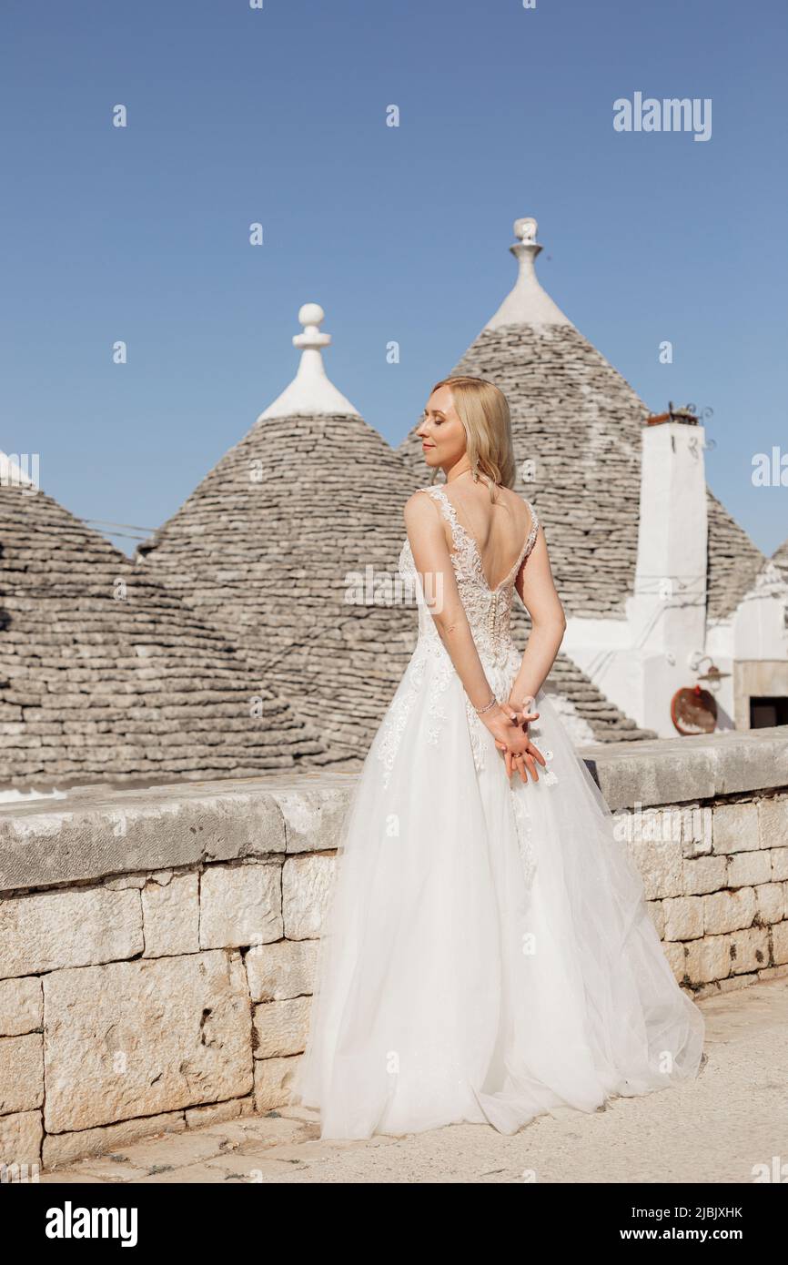 Porträt einer jungen blonden Braut in weißem Hochzeitskleid genießen und posieren in der Nähe der alten Stadt Stein Pyramiden in Italien Rückansicht, städtischen Hintergrund. Wunderschön Stockfoto