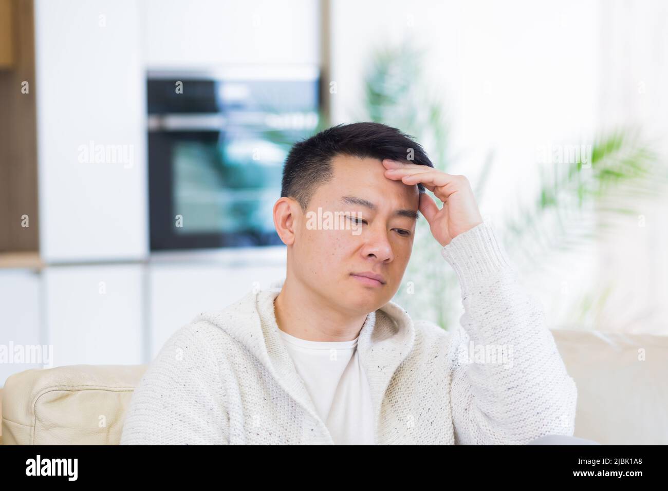 Gelangweilte Freunde junger asiatischer Mann, der allein zu Hause auf dem Sofa sitzt. Vermisst Mann sitzt auf der Couch in der Wohnung. Einsamer Kerl im Wohnzimmer. Ich hatte mir Sorgen gemacht Stockfoto