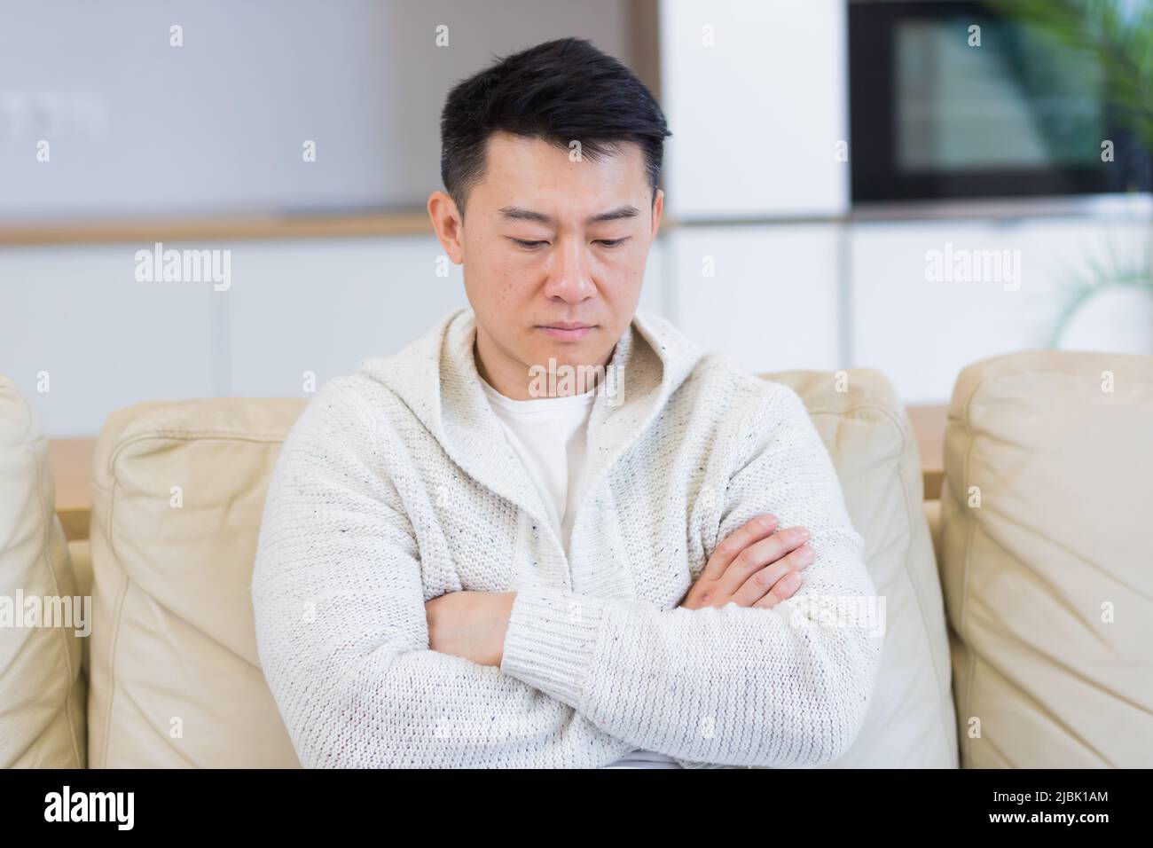 Gelangweilte Freunde junger asiatischer Mann, der allein zu Hause auf dem Sofa sitzt. Vermisst Mann sitzt auf der Couch in der Wohnung. Einsamer Kerl im Wohnzimmer. Ich hatte mir Sorgen gemacht Stockfoto