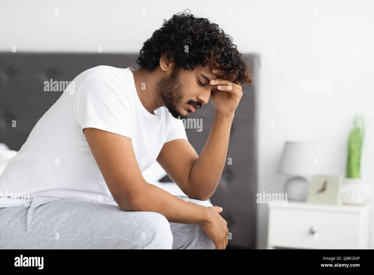 Deprimierter indischer Kerl, der zu Hause auf dem Bett sitzt Stockfoto