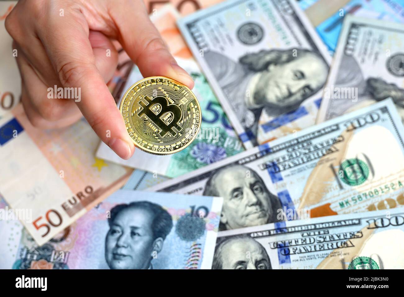 Bitcoin in weiblicher Hand auf dem Hintergrund von US-Dollar-, Euro- und Yuan-Banknoten. Elektronisches dezentrales Geld, Wechselkurs Stockfoto