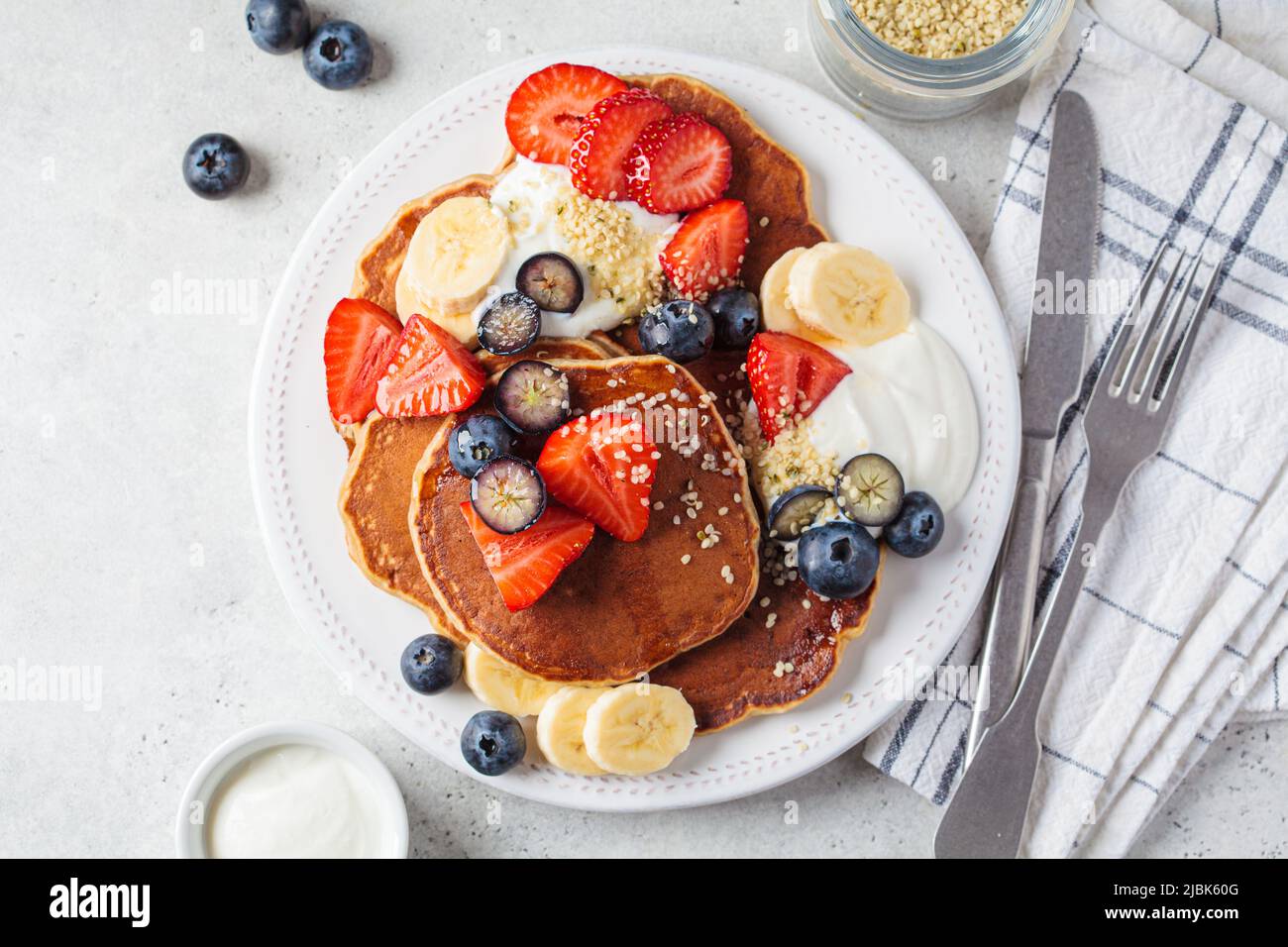 Sommerfrühstück. Pfannkuchen mit Erdbeeren, Blaubeeren, Banane und Rahm auf einem weißen Teller, Draufsicht. Veganes Rezept. Stockfoto