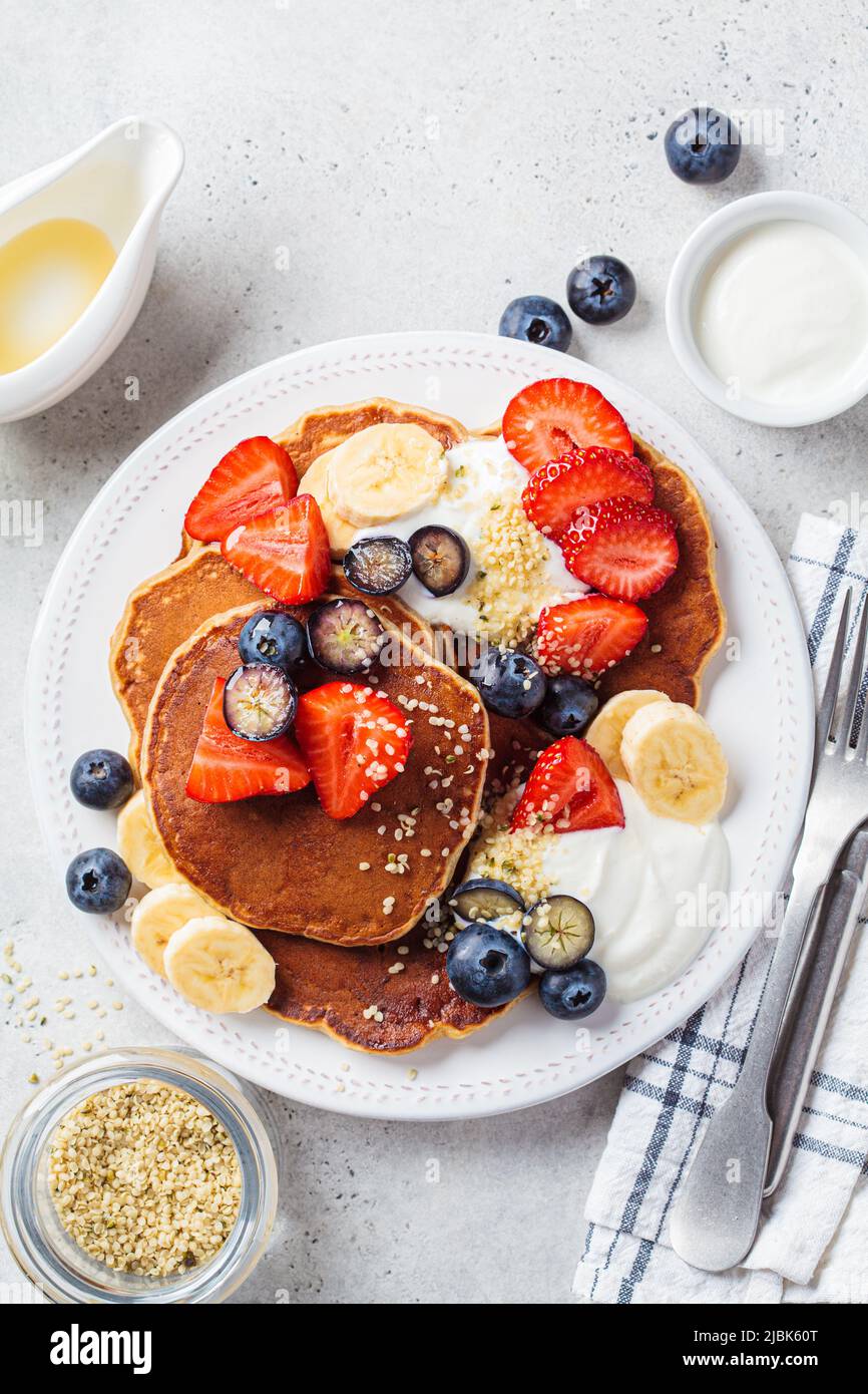 Sommerfrühstück. Pfannkuchen mit Erdbeeren, Blaubeeren, Banane und Rahm auf einem weißen Teller, Nahaufnahme. Veganes Rezept. Stockfoto