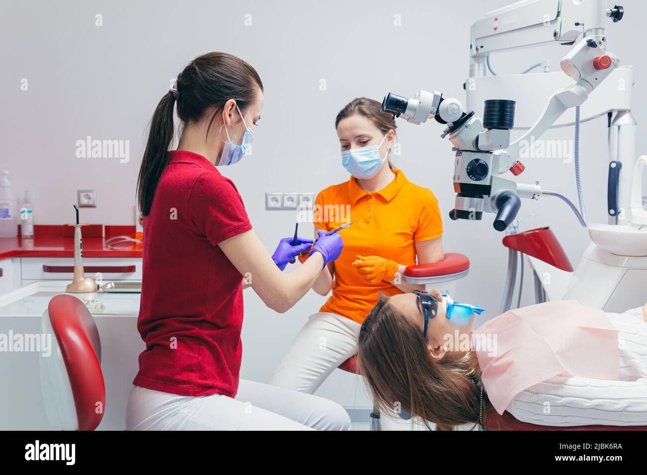 Junge schöne Patientin in der Zahnarztpraxis behandelt Zähne, liegt auf einem Zahnstuhl, Arzt und Assistent behandelt die Zähne des Patienten in Masken, glo Stockfoto