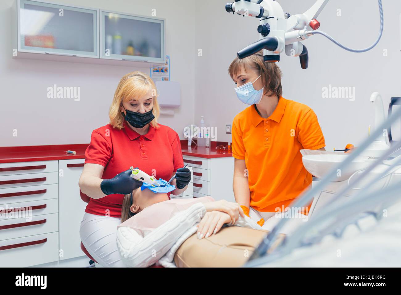 Junge schöne Patientin in der Zahnarztpraxis behandelt Zähne, liegt auf einem Zahnstuhl, Arzt und Assistent behandelt die Zähne des Patienten in Masken, glo Stockfoto