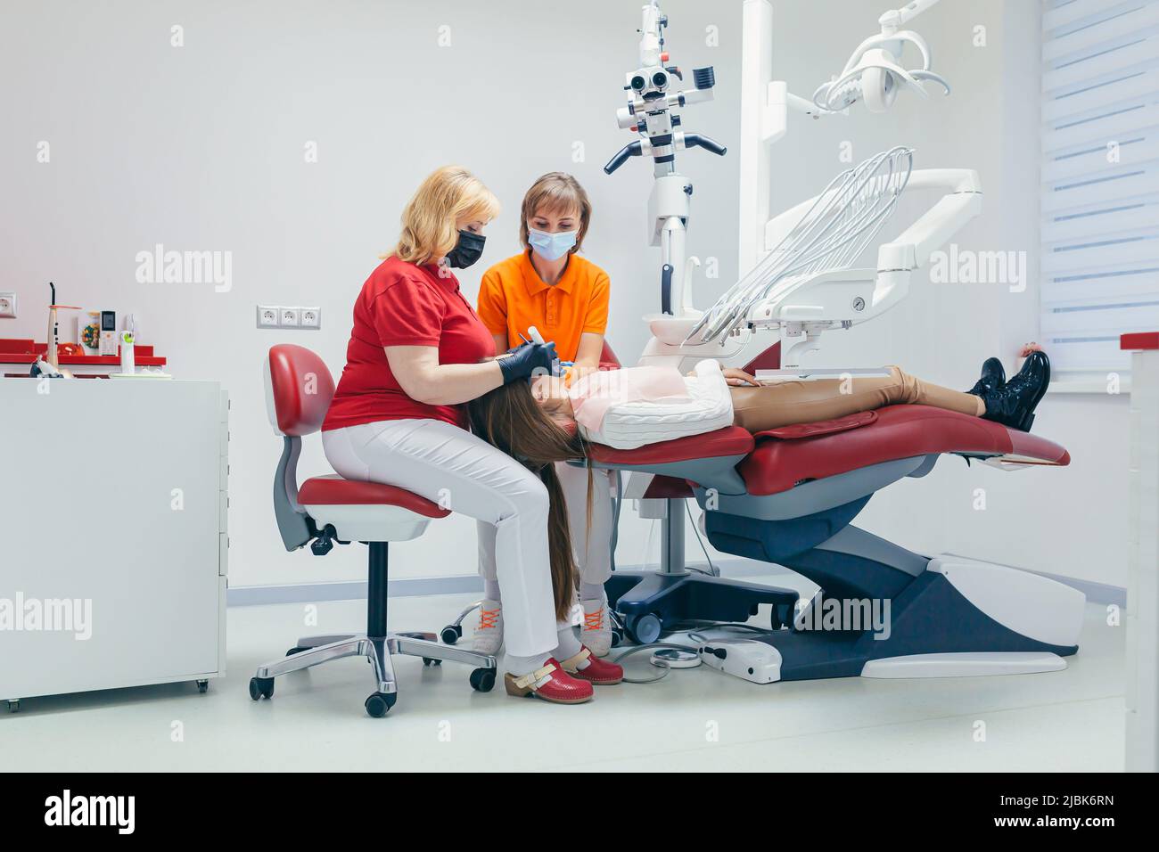 Junge schöne Patientin in der Zahnarztpraxis behandelt Zähne, liegt auf einem Zahnstuhl, Arzt und Assistent behandelt die Zähne des Patienten in Masken, glo Stockfoto