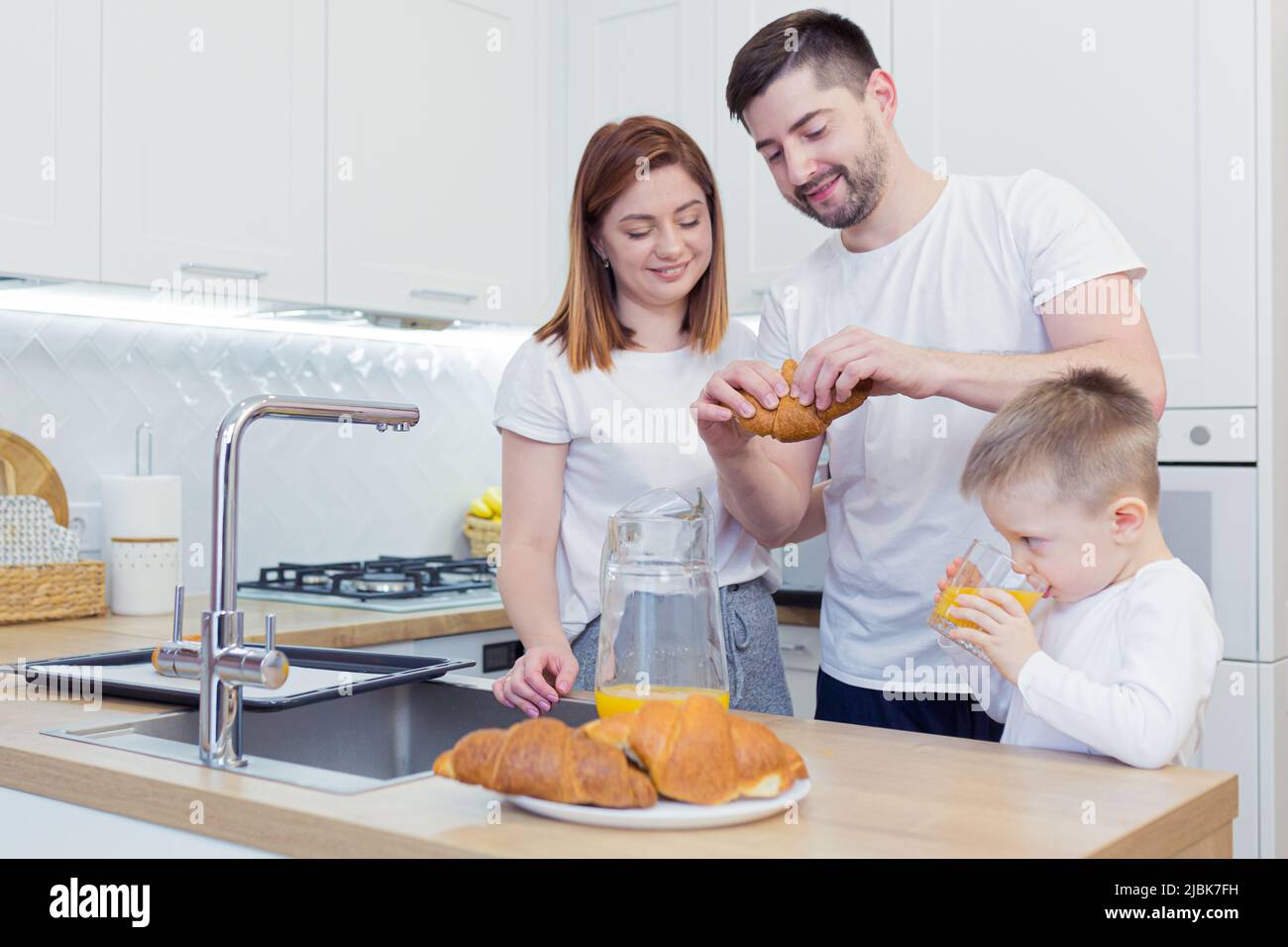 Familienfrühstück, Mama, Papa, zwei Kinder, Jungen, die von Mama gebackene Croissants aßen, Kaffee und frischen Saft tranken, lächelten und sich zu Hause in der Kitch umarmten Stockfoto