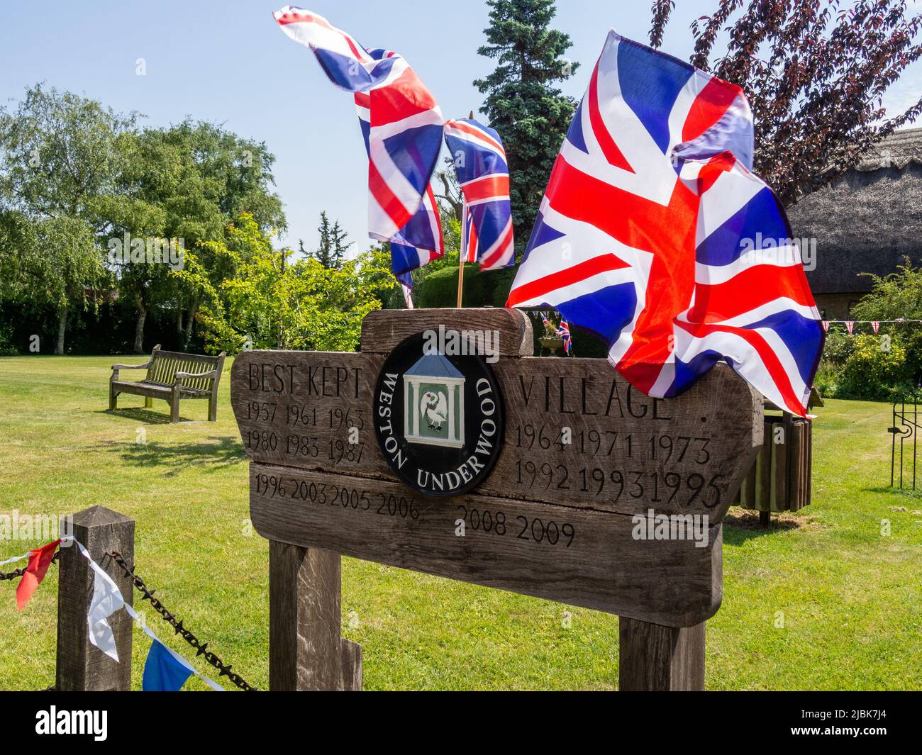 Holzschild für das Dorf Weston Underwood, Buckinghamshire, Großbritannien; geschmückt mit Union Jack Flaggen zur Feier der Platinum Jublee 2022 Stockfoto