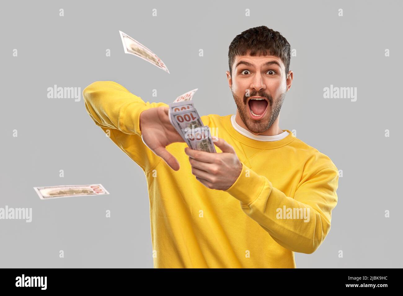 Glücklicher Mann im gelben Sweatshirt, der Geld wirft Stockfoto