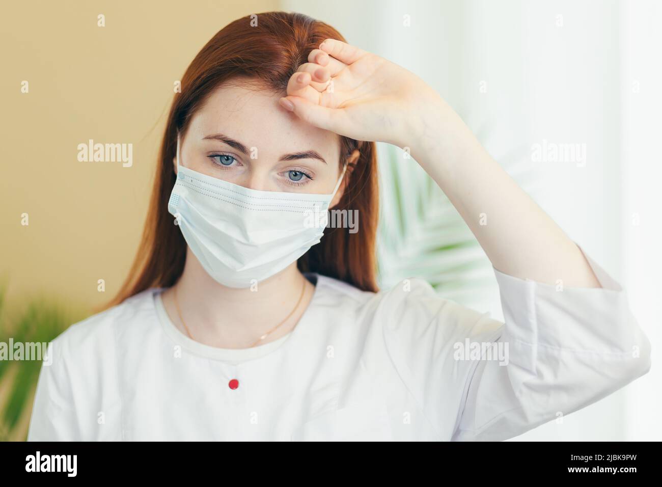 Müde Frau Arzt in medizinische Schutzmaske auf Gesicht Hand hinter dem Kopf halten Stockfoto