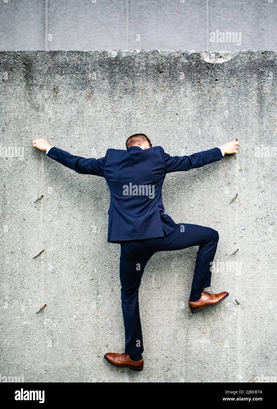 Ein verkleideter junger Mann, der eine Betonwand klettert und nur einen freiliegenden Stahl in der Hand hält. Stockfoto