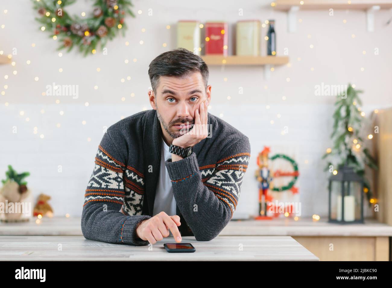 Ein Mann mit einem Bart ist gelangweilt und ist zu Weihnachten allein zu Hause und schaut in Depressionen auf das Telefon Stockfoto