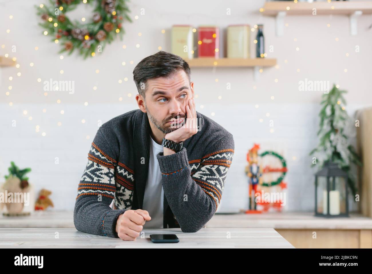 Ein Mann mit einem Bart ist gelangweilt und ist zu Weihnachten allein zu Hause und schaut in Depressionen auf das Telefon Stockfoto