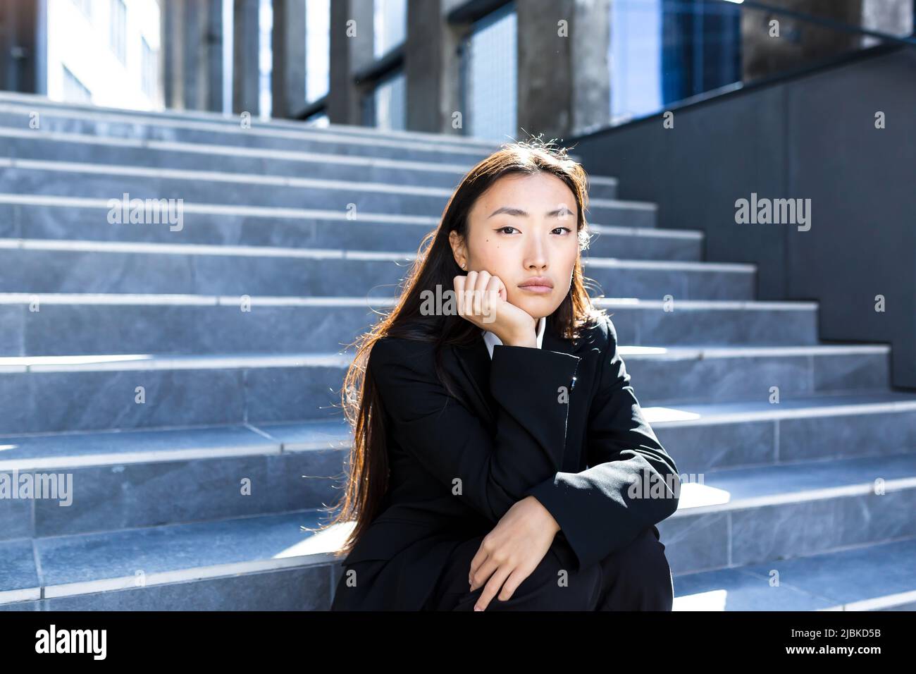 Junge schöne asiatische Frau verärgert und traurig auf der Treppe des Bürozentrums sitzend, entließ depressive Geschäftsfrau Stockfoto