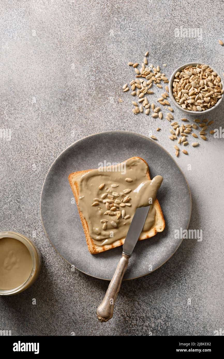 Knuspriges Brot mit hausgemachter Sonnenblumensamenbutter auf grauem Hintergrund. Kochen Nuss kostenloses veganes Frühstück. Blick von oben. Vertikales Format. Stockfoto