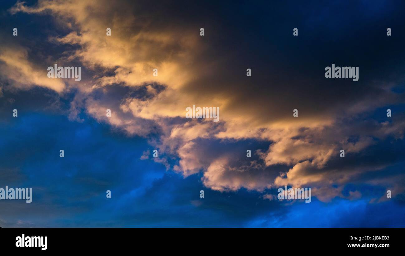 Beleuchtete Wolken beim Sonnenuntergang , mit großem Kontrast der dunklen Wolken im Hintergrund und dem dunkelblau Himmel Stockfoto