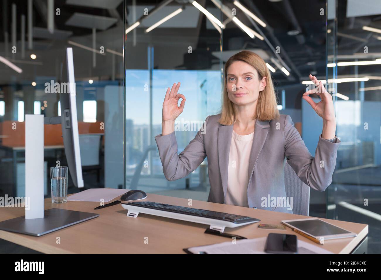 Erfolgreiche Geschäftsfrau in Geschäftskleidung, meditierend bei der Arbeit in einem modernen Büro am Computer, versuchend, Ruhe und Balance zu halten Stockfoto