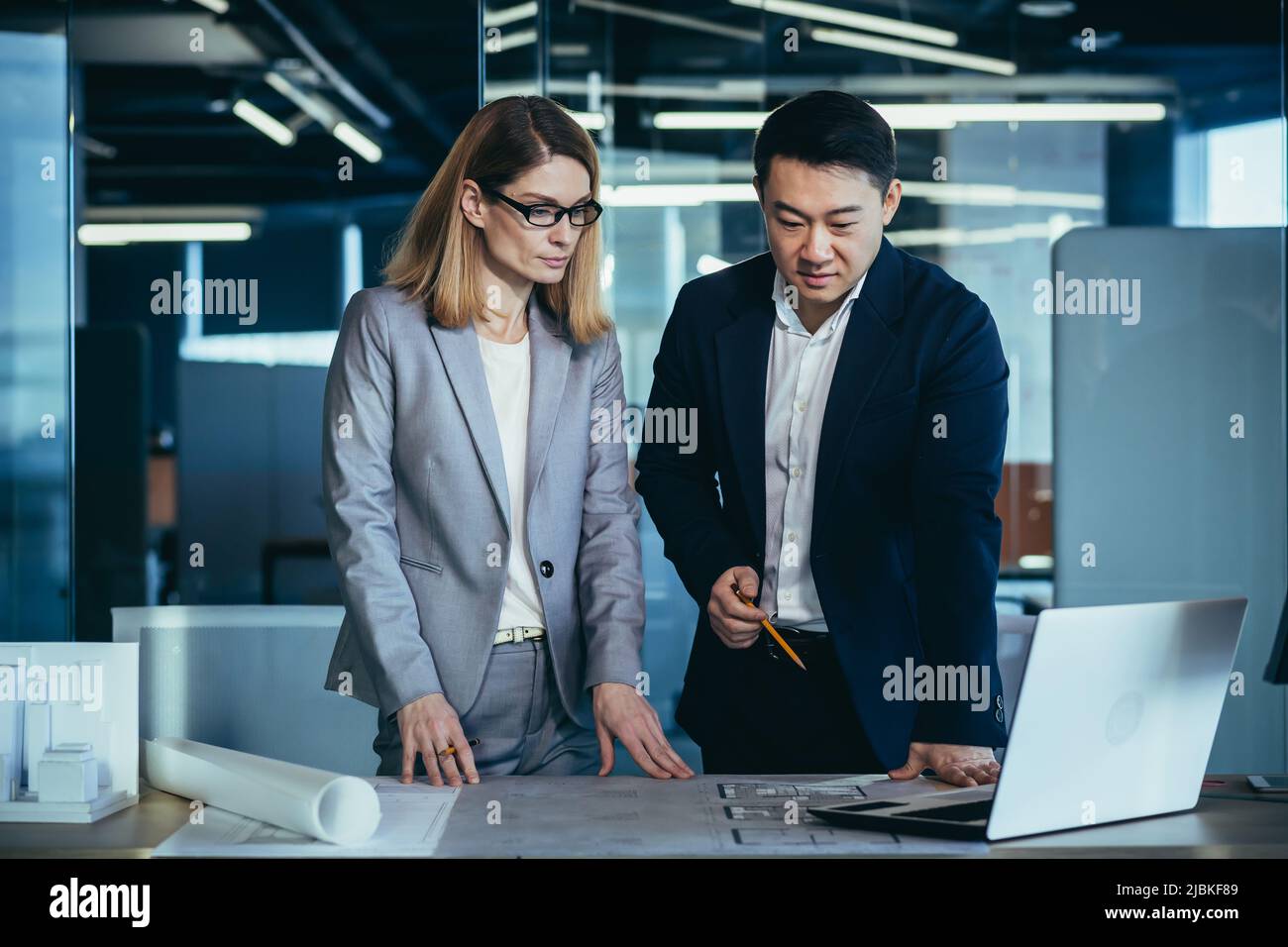 Ein Team aus multirassischen Geschäftsarchitekten und Designern diskutiert die Erstellung eines Projektentwurfs, indem sie sich den Bildschirm eines Laptops und einen Computertisch anschaut. Stockfoto