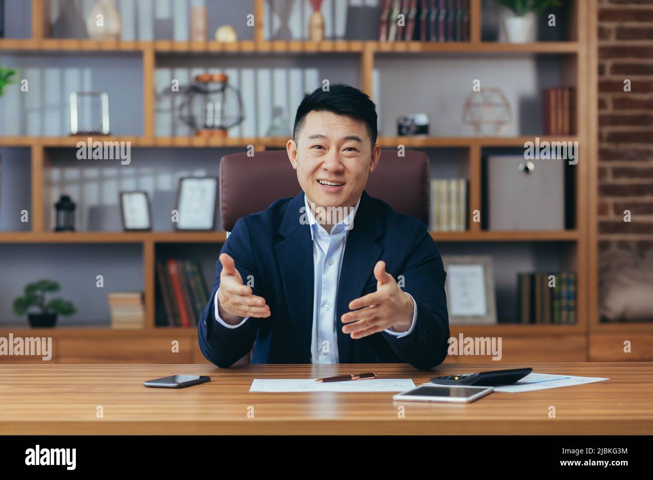 Fröhlicher Geschäftsmann Blick auf Webcam, lächelnd und frohlockende Geste gerne Hände, Online-Konferenz-Meeting, erfolgreiche asiatische Stockfoto