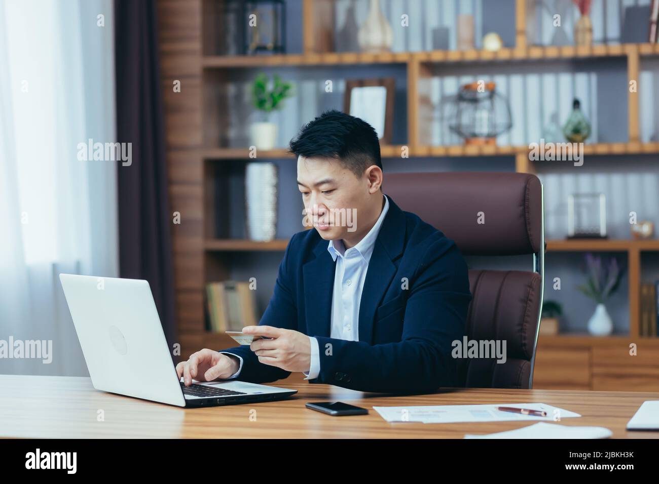 Der erfolgreiche asiatische Geschäftsmann führt Bankgeschäfte durch und überweist Geld von einem elektronischen Konto, verwendet einen Laptop und eine Bankkreditkarte Stockfoto