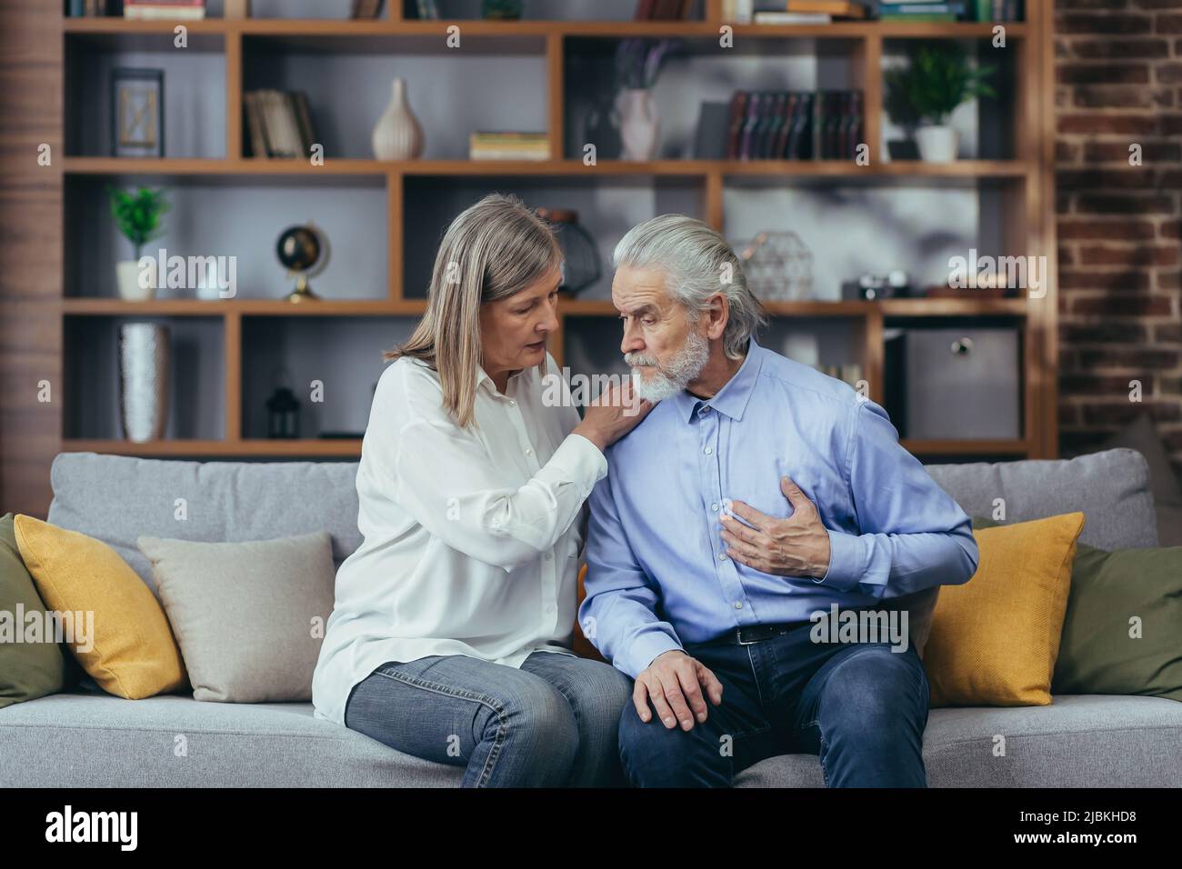 Ältere reife Frau, die ihrem Mann bei Brustschmerzen hilft. Alter Mann, der schlechte Schmerzkrankheit fühlt. Ehefrau, die Ehemann unterstützt - älteres Paar, das an Sym leidet Stockfoto