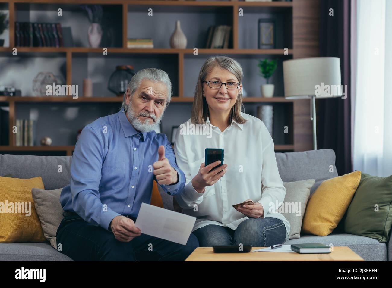 Ältere Familienpaar, grauhaarige ältere zahlen, Dienste geben Datendokumente mit Anwendung Handy-Kreditkarte. Rentner zu Hause. Stockfoto