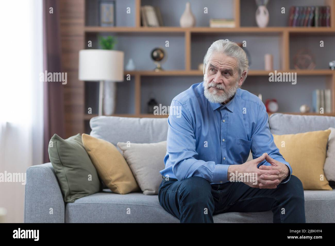 Älterer nachdenklicher Mann, der auf dem Sofa sitzt, einsamer grauhaariger Mann im Wohnzimmer, deprimiert Stockfoto