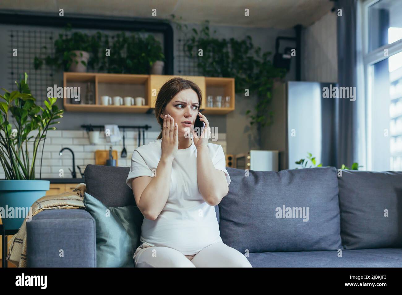 Traurige, schwanger Frau zu Hause ängstlich am Telefon auf der Couch sitzend Stockfoto