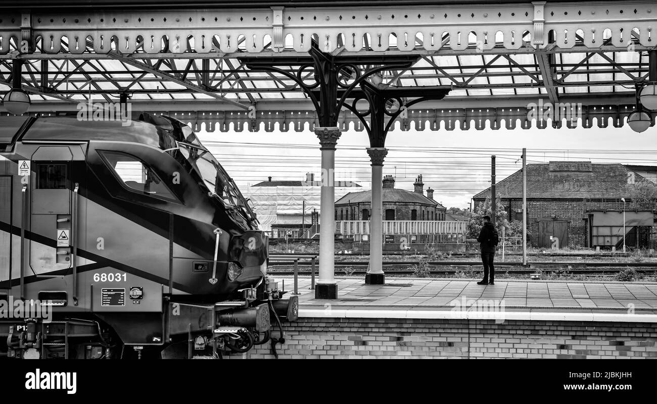 Eine moderne Lokomotive ruht auf einer Bahnhofsplattform und ein einflüchtiger Passagier steht unter einem historischen Vordach. Stockfoto